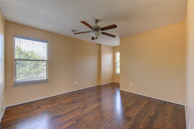 an empty room with wooden floor ceiling fan and windows