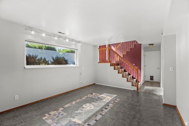 11934 South Cedar Ridge Road Sandy, UT 84094 - Photo 24 of 58 Spacious room featuring tile flooring with decorative inlay, a wide window, track lighting, and a prominent staircase with wood handrails