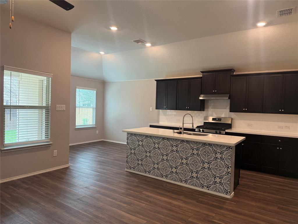 1004 Rising Moon Drive Fort Worth, TX 76052 - Photo 4 of 13 Open-concept kitchen featuring dark wood cabinetry, white countertops, a patterned island facade, stainless steel gas range with overhead ventilation, and recessed lighting