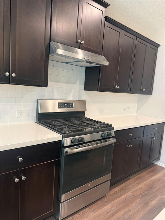 1004 Rising Moon Drive Fort Worth, TX 76052 - Photo 7 of 13 Stainless steel range with a gas cooktop, dark wood cabinetry, white subway tile backsplash, light-colored countertops, and wood-finish flooring