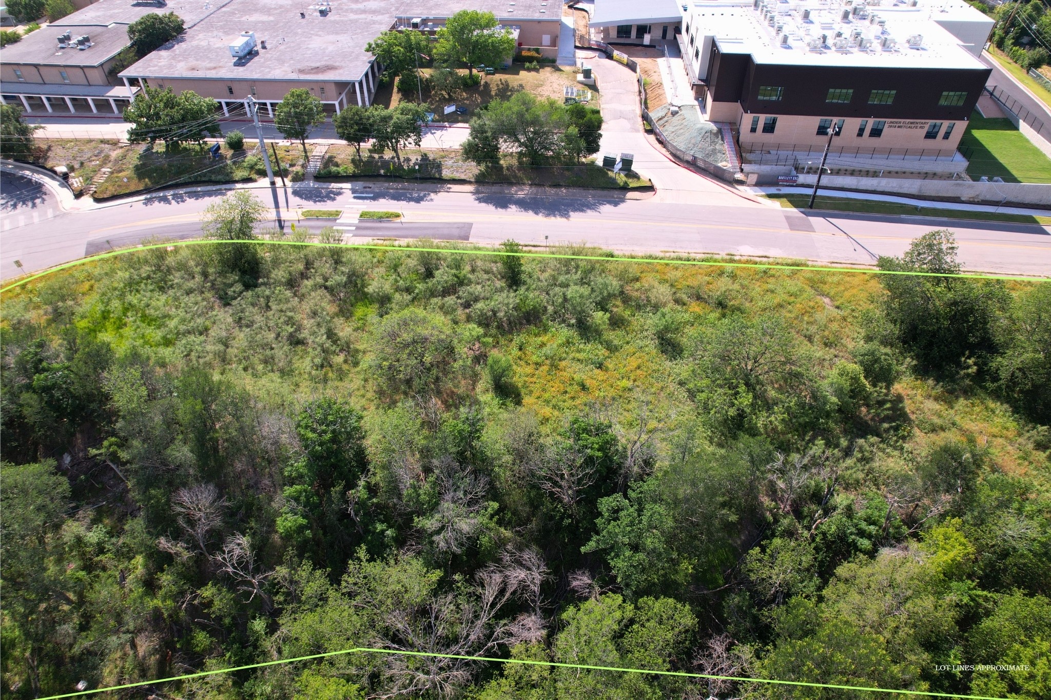 2813-2827 Metcalfe Road Austin, TX 78741 - Photo 11 of 13 A spacious, undeveloped lot with abundant natural growth, bordered by a curving road and urban structures.