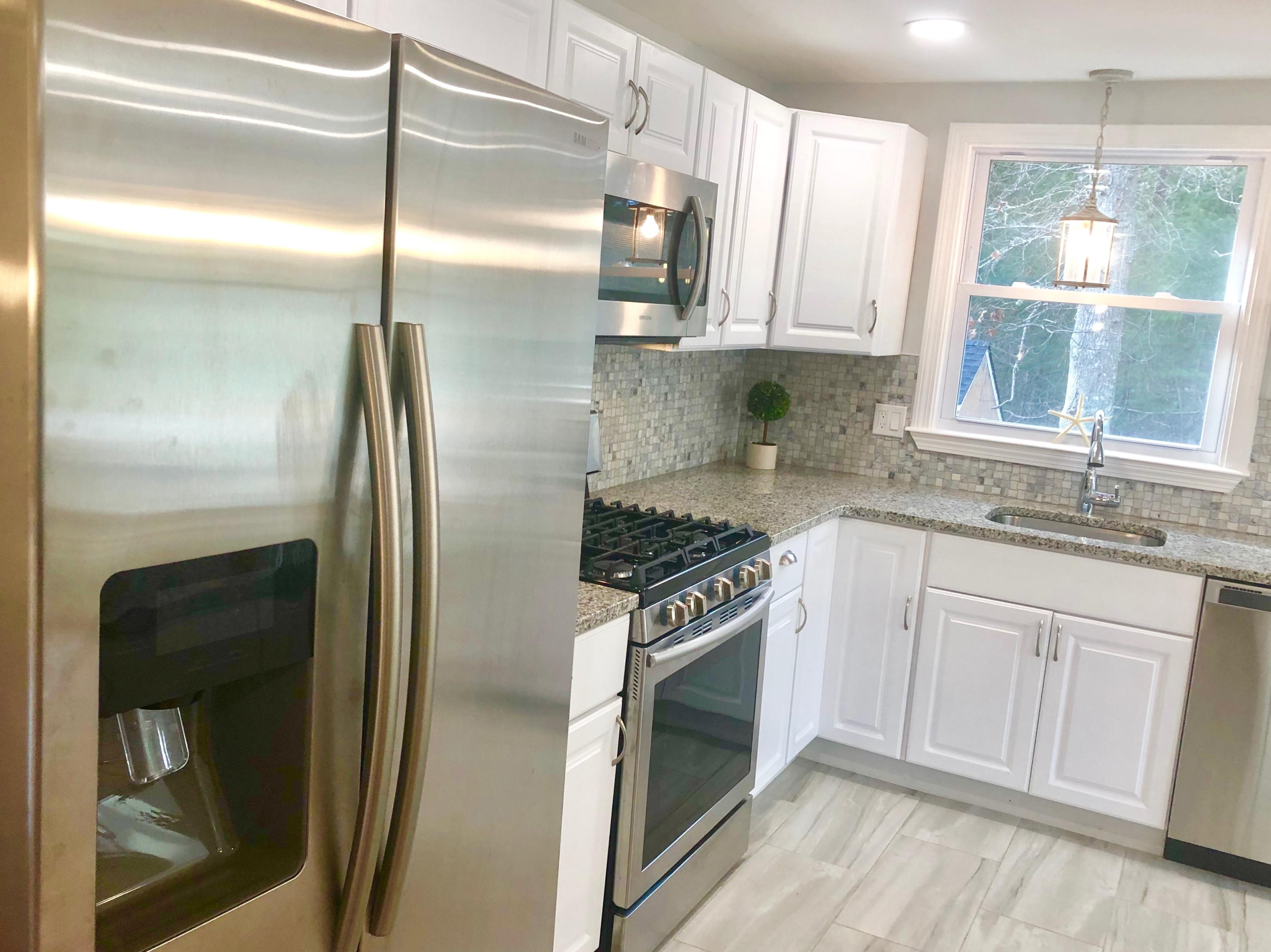 57 Stage Coach Road Centerville, MA 02632 - Photo 3 of 34 a kitchen with stainless steel appliances granite countertop a refrigerator a sink a stove and white cabinets with wooden floor