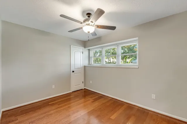 an empty room with wooden floor fan and windows