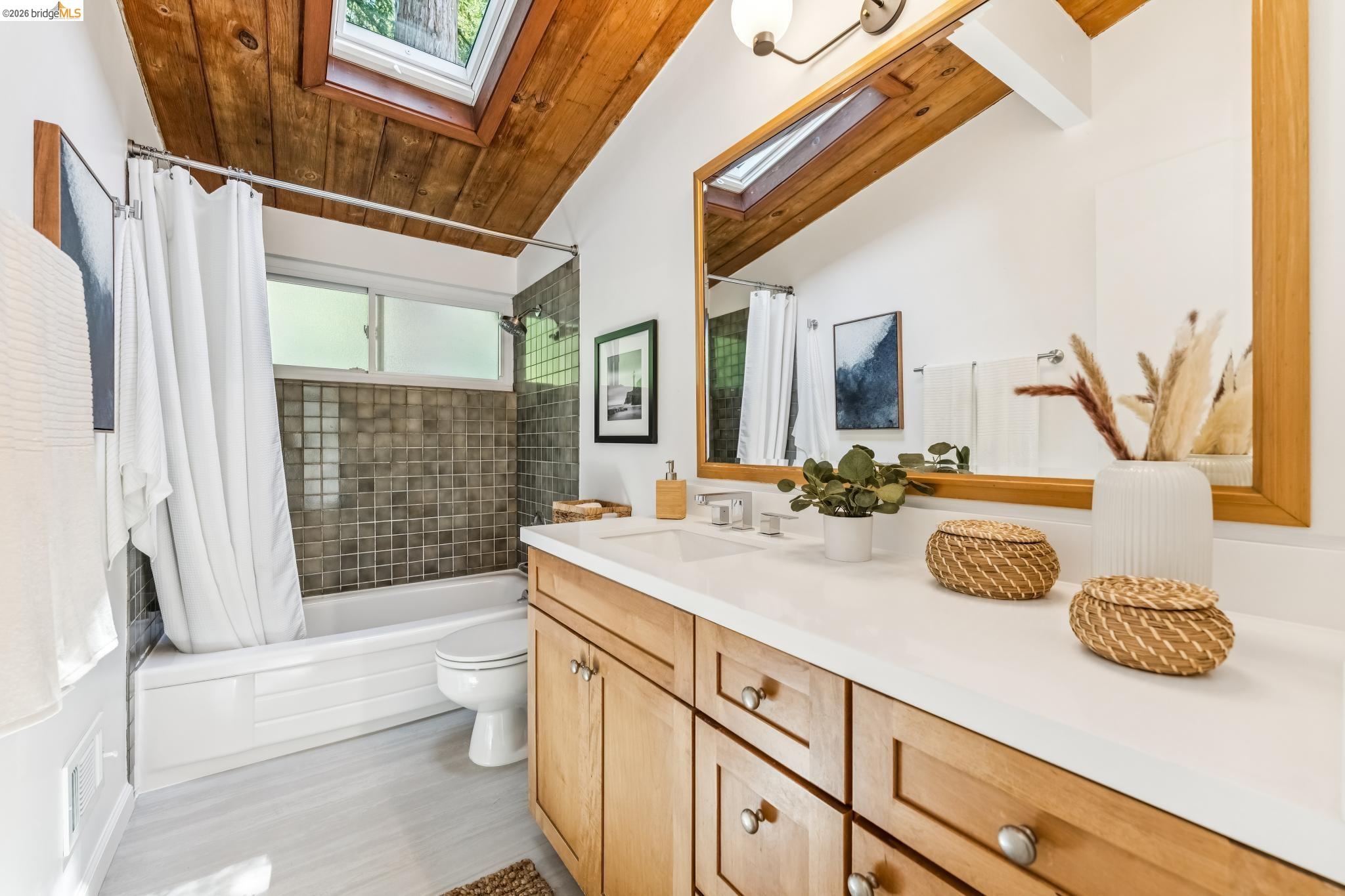 6645 Heather Ridge Way Oakland, CA 94611 - Photo 27 of 61 Wood-paneled vaulted ceiling with skylights, double vanity with light wood cabinetry, white countertop, and integrated sinks