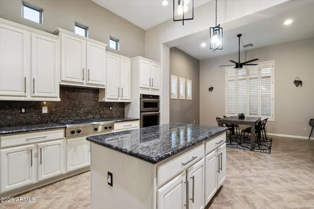 a kitchen with stainless steel appliances kitchen island granite countertop a dining table chairs and a refrigerator