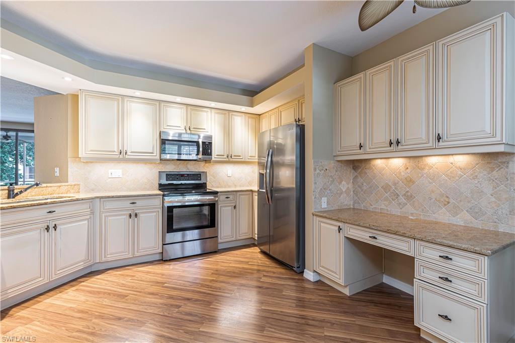 6914 Satinleaf Road North, Unit 102 Naples, FL 34109 - Photo 2 of 24 Kitchen featuring appliances with stainless steel finishes, light wood-style flooring, light stone counters, ceiling fan, and tasteful backsplash