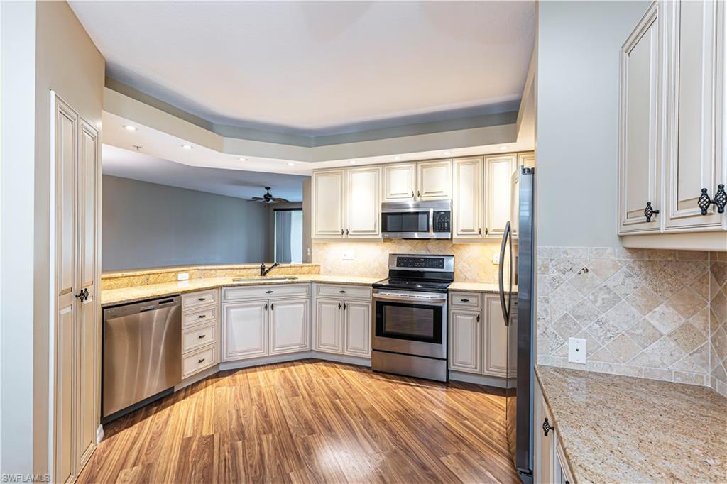 6914 Satinleaf Road North, Unit 102 Naples, FL 34109 - Photo 3 of 24 Kitchen featuring appliances with stainless steel finishes, light wood-style floors, a tray ceiling, recessed lighting, and tasteful backsplash
