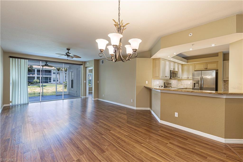 6914 Satinleaf Road North, Unit 102 Naples, FL 34109 - Photo 5 of 24 Unfurnished living room with a chandelier, wood finished floors, ceiling fan, and a tray ceiling