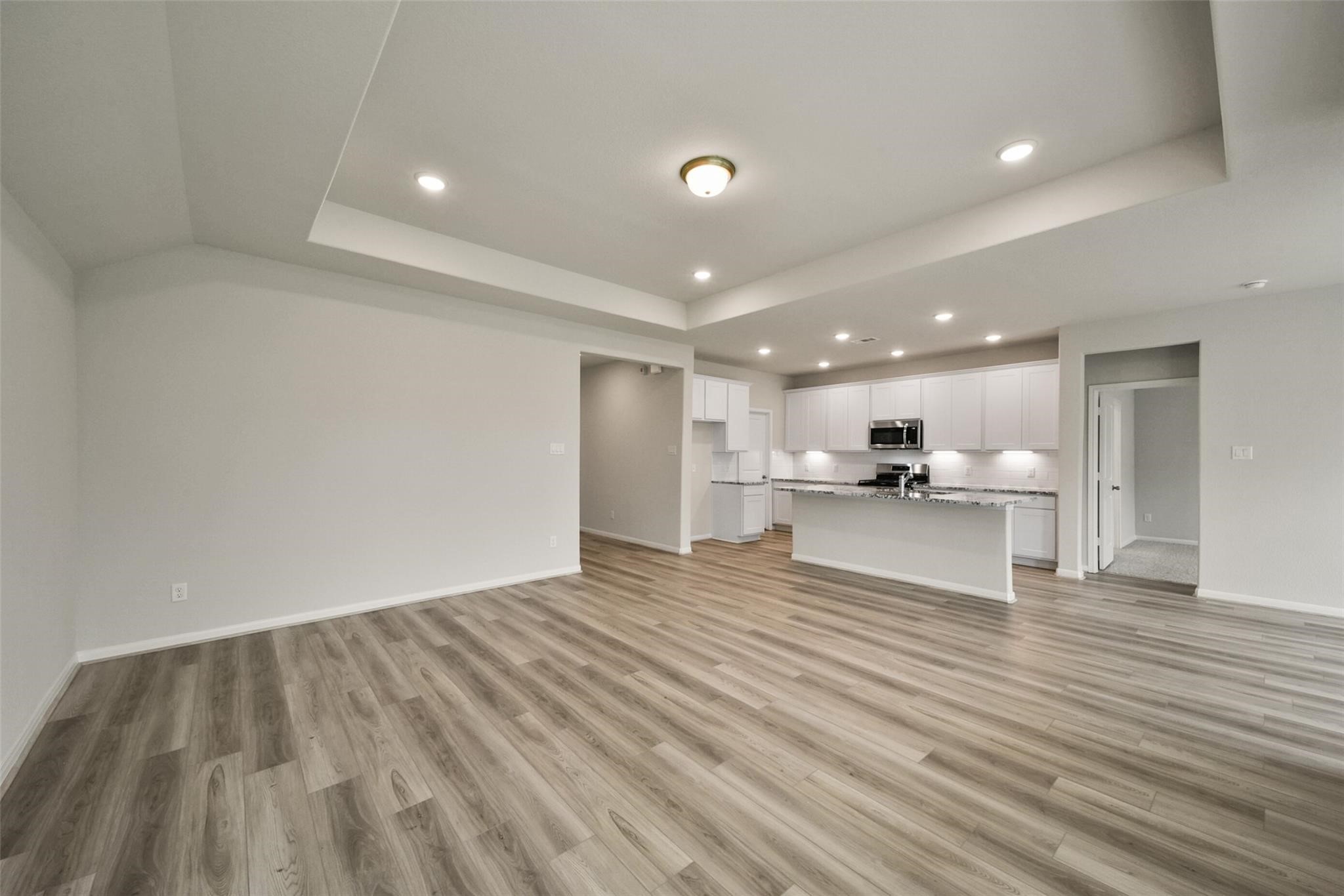 10522 Plumas Run Drive Rosharon, TX 77583 - Photo 5 of 29 This photo showcases a spacious, open-concept living area with modern wood flooring and a bright kitchen featuring white cabinetry, granite countertops, and stainless steel appliances. The recessed lighting and neutral walls add a touch of elegance, creating a welcoming and versatile space.