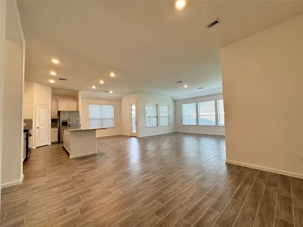 a view of an empty room and kitchen with wooden floor
