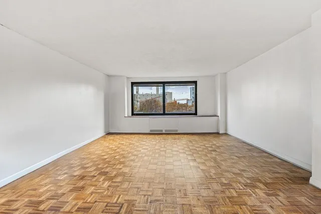 a view of an empty room with window and wooden floor
