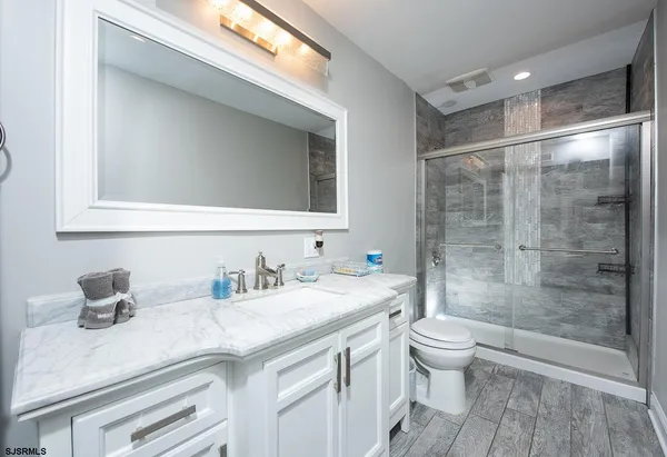 a bathroom with a granite countertop sink a toilet a mirror and shower