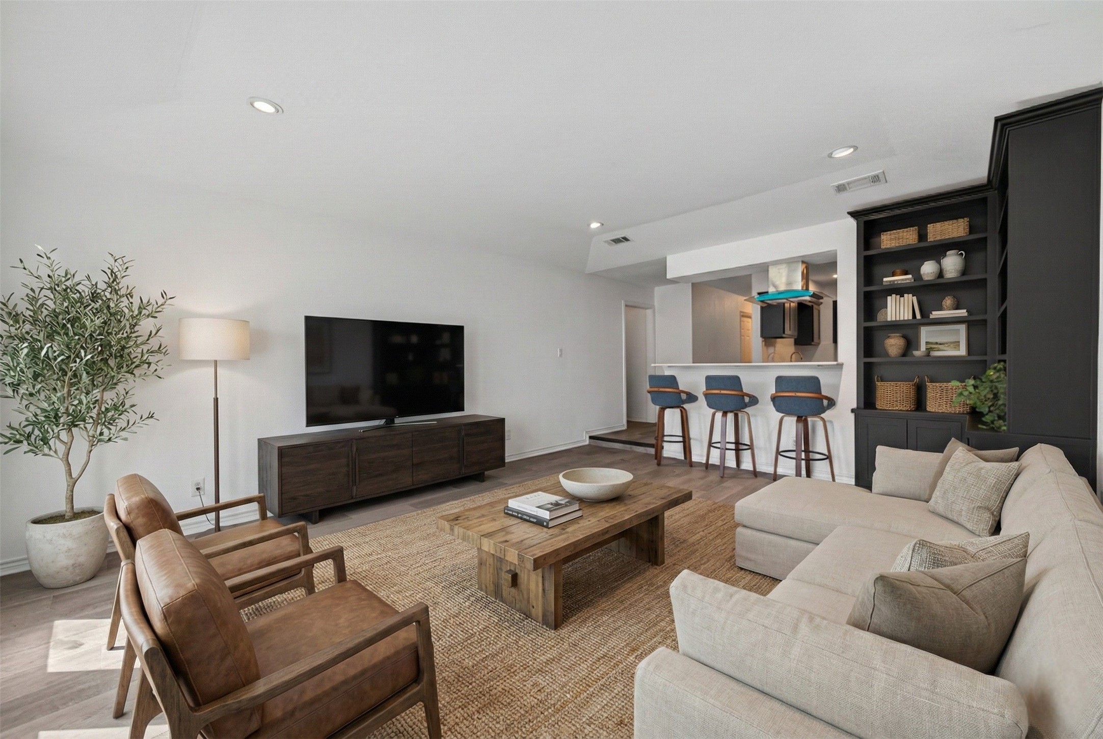 15335 Robin Trail Conroe, TX 77302 - Photo 11 of 38 Inviting open-concept virtually staged living area with excellent sightlines to the kitchen and dining spaces. The expansive room features recessed lighting, built-in shelving for organization, and modern wood-look flooring that flows throughout the home. Large windows and French doors provide abundant natural light and showcase the peaceful backyard views.