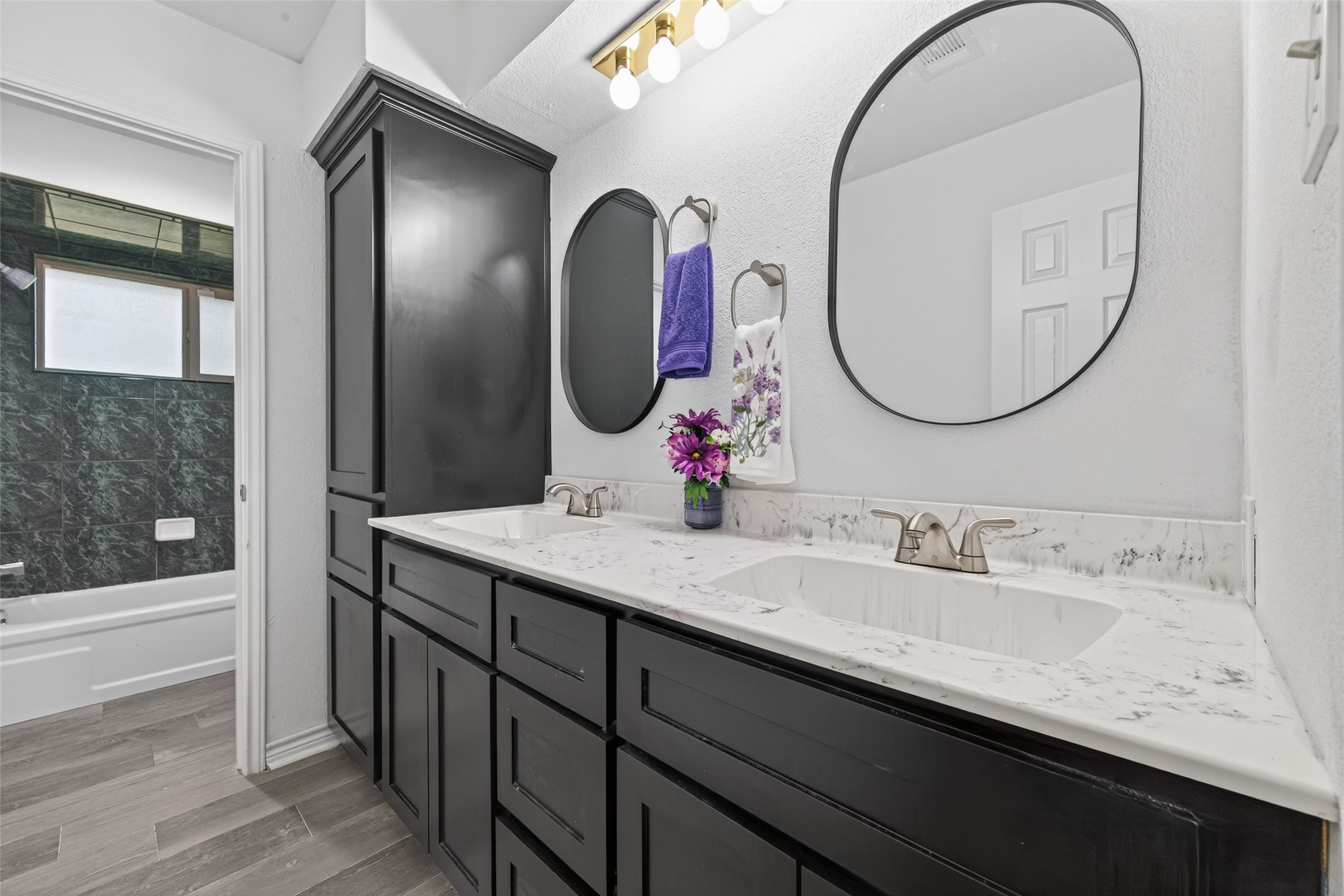 15335 Robin Trail Conroe, TX 77302 - Photo 29 of 38 Updated secondary bathroom featuring a spacious dual-sink vanity with modern cabinetry, updated fixtures, and elegant countertops. The well-designed layout includes a separate water closet for privacy and a shower/tub combination with designer tile surround. Stylish lighting, large mirrors, and durable wood-look flooring complete this functional and attractive bathroom.