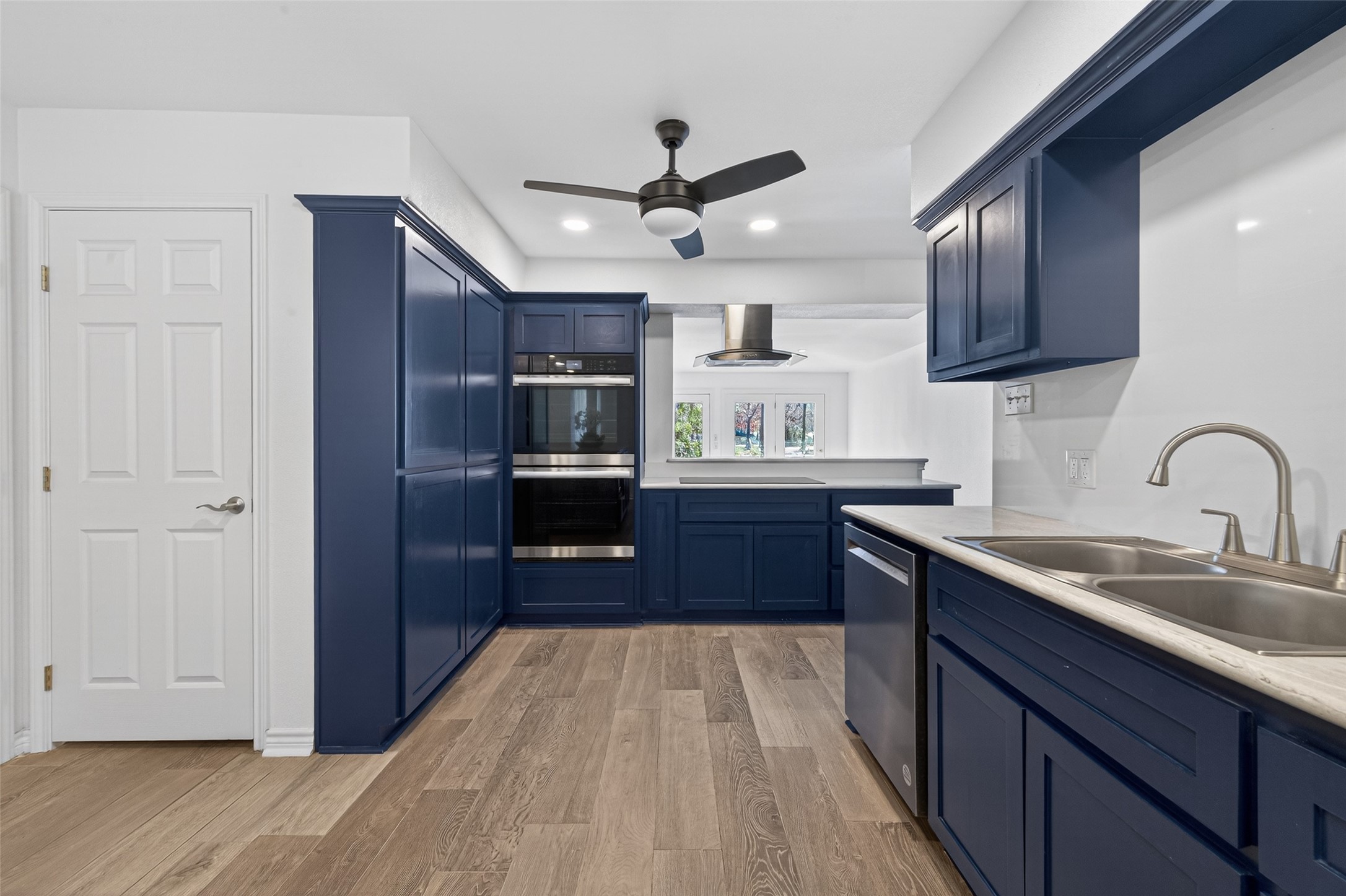 15335 Robin Trail Conroe, TX 77302 - Photo 6 of 38 Stunning fully renovated kitchen featuring rich navy blue custom cabinetry with sleek hardware, new 2025 appliances including double ovens, and elegant light-toned quartz countertops. Beautiful wood-look flooring flows throughout, complemented by modern recessed lighting and a stylish ceiling fan. The bright, open layout offers excellent workspace and storage.