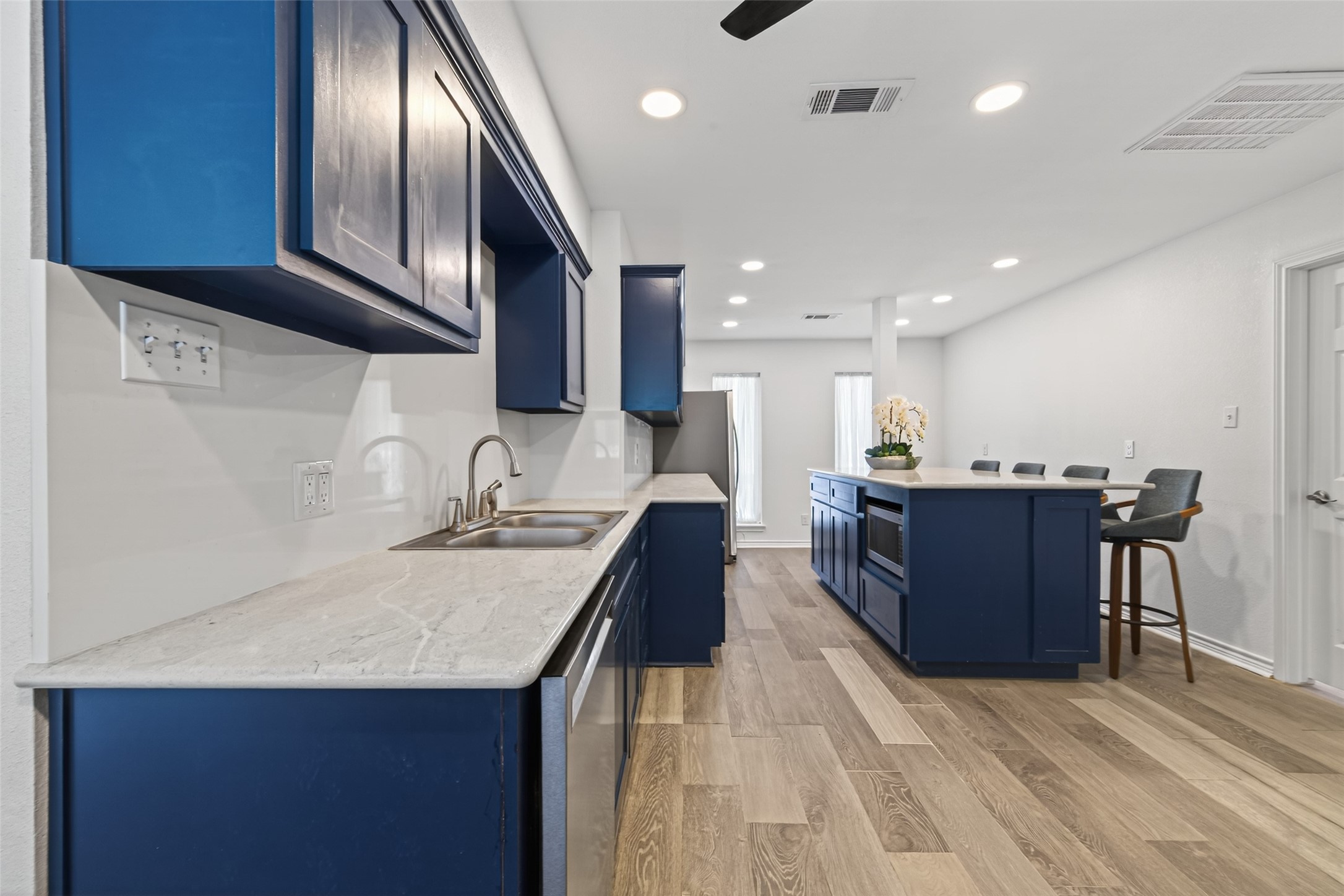 15335 Robin Trail Conroe, TX 77302 - Photo 7 of 38 Expansive renovated kitchen showcasing a generous center island with seating for casual dining and entertaining. The sophisticated navy cabinetry extends throughout, paired with tiled backsplash and modern light fixtures. Open sightlines create an ideal layout for gatherings, while abundant counter space and storage make this kitchen as functional as it is beautiful.