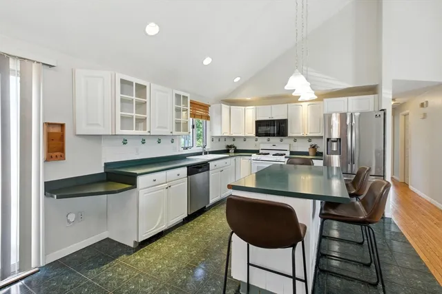 a kitchen with stainless steel appliances granite countertop a sink a stove a refrigerator cabinets and a dining table with wooden floor