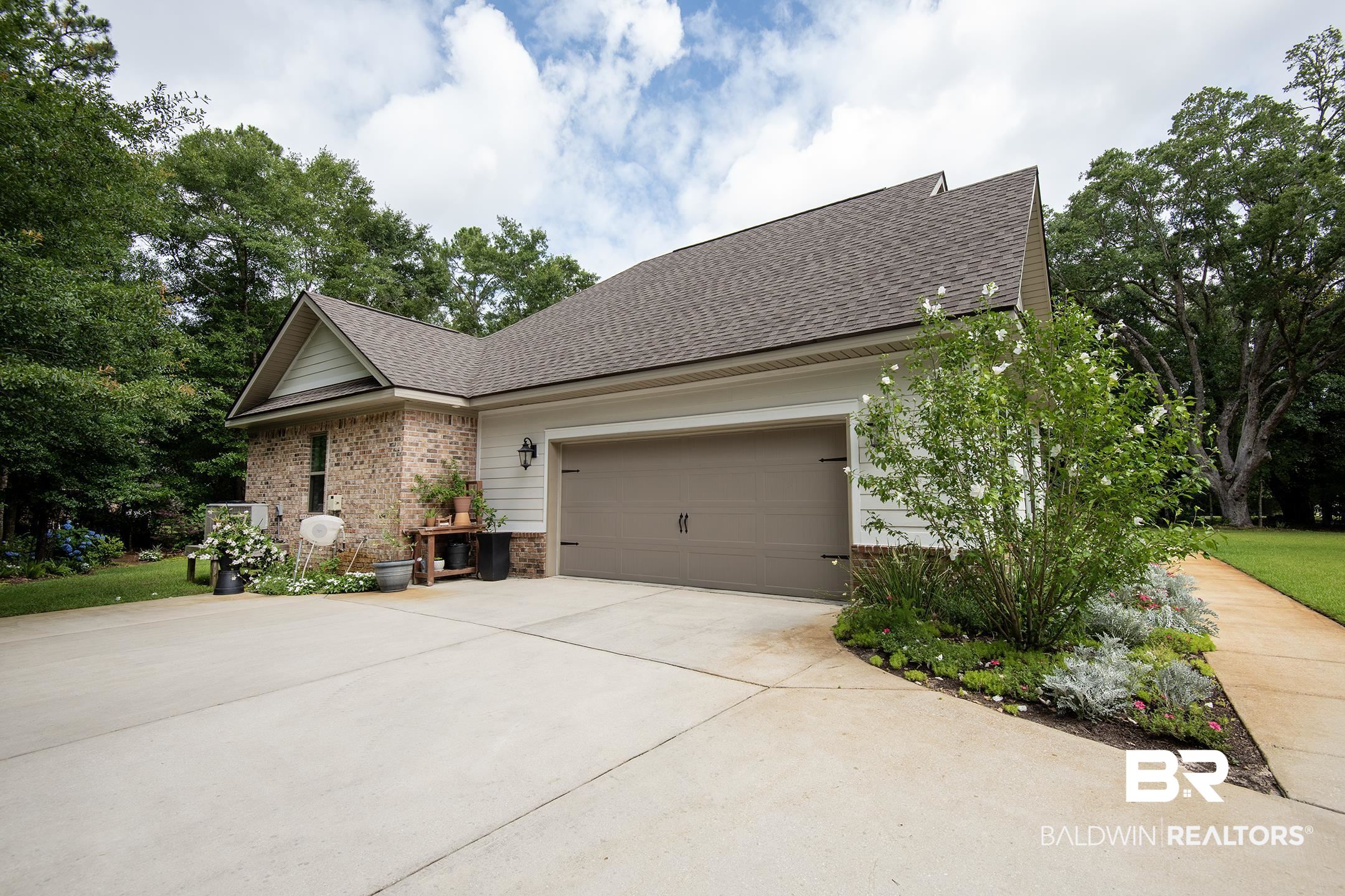 18754 Treasure Oaks Road Gulf Shores, AL 36542 - Photo 40 of 53 Attached two-car garage with a taupe overhead door and decorative hardware, brick and siding exterior, shingled roof, and mature perimeter trees