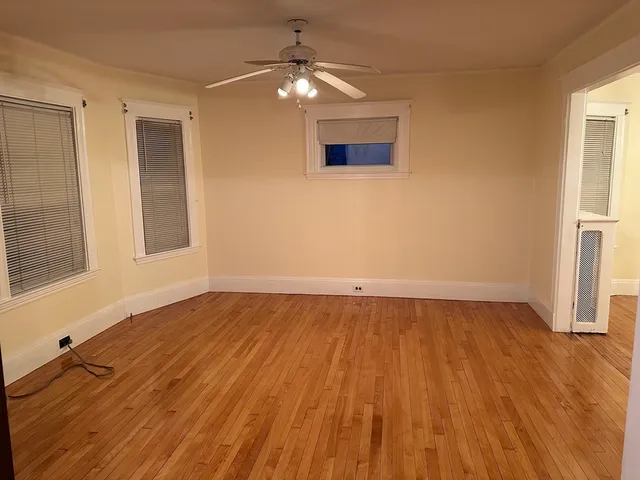 an empty room with wooden floor chandelier fan and windows