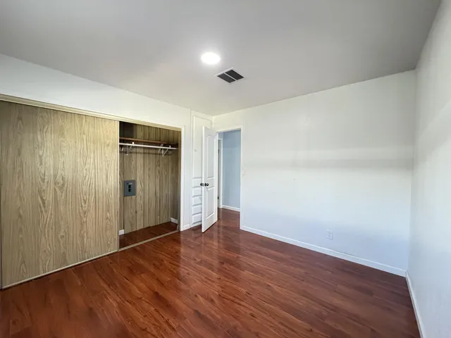 a view of an empty room with wooden floor and closet