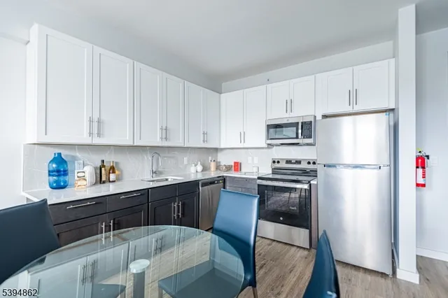 a kitchen with stainless steel appliances a refrigerator a stove a sink dishwasher and white cabinets with wooden floor