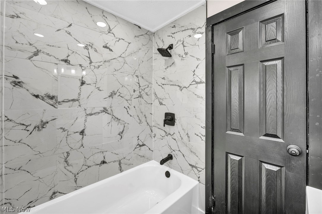 7339 River Road Olmsted Falls, OH 44138 - Photo 27 of 45 Bathtub with large format marble-look tile surround featuring dark bronze fixtures, recessed lighting, and a paneled door
