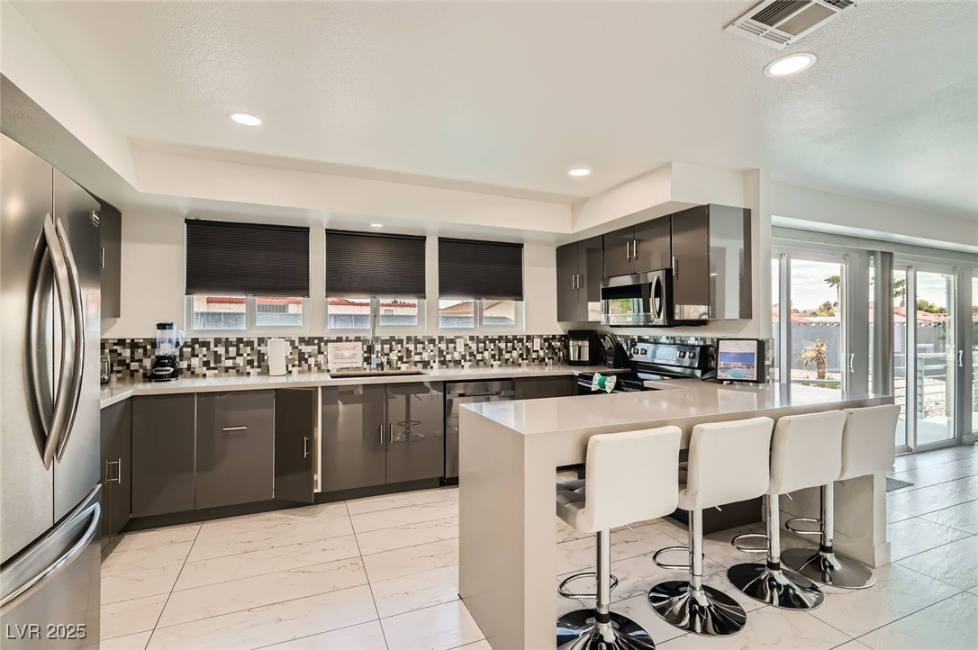 2520 Castlesands Way Las Vegas, NV 89121 - Photo 12 of 59 Kitchen with a kitchen breakfast bar, stainless steel appliances, decorative backsplash, light countertops, and recessed lighting