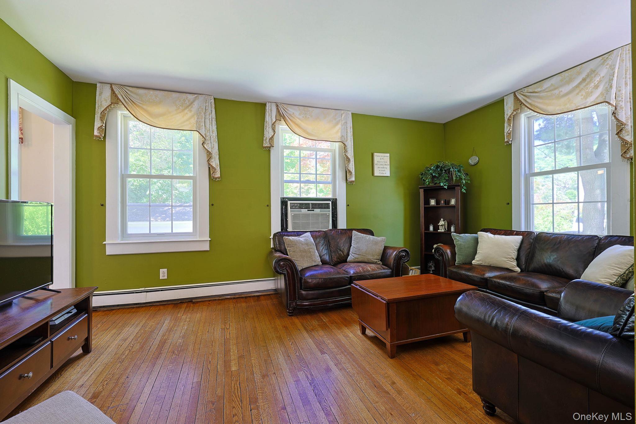 9 Library Road Tuxedo Park, NY 10987 - Photo 5 of 37 Wood-finish flooring throughout, featuring multiple double-hung windows with white trim, baseboard heating, and a built-in shelf unit