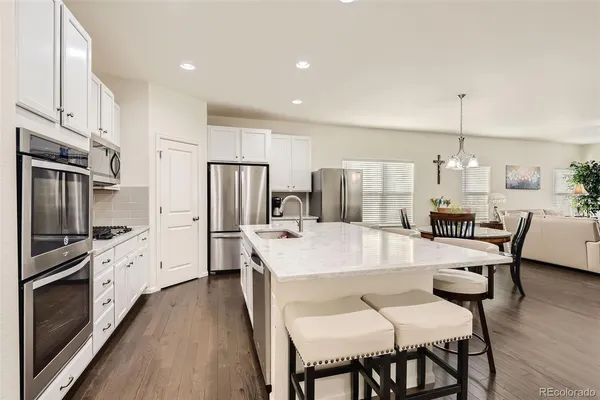 a kitchen with stainless steel appliances kitchen island granite countertop a dining table chairs refrigerator and microwave