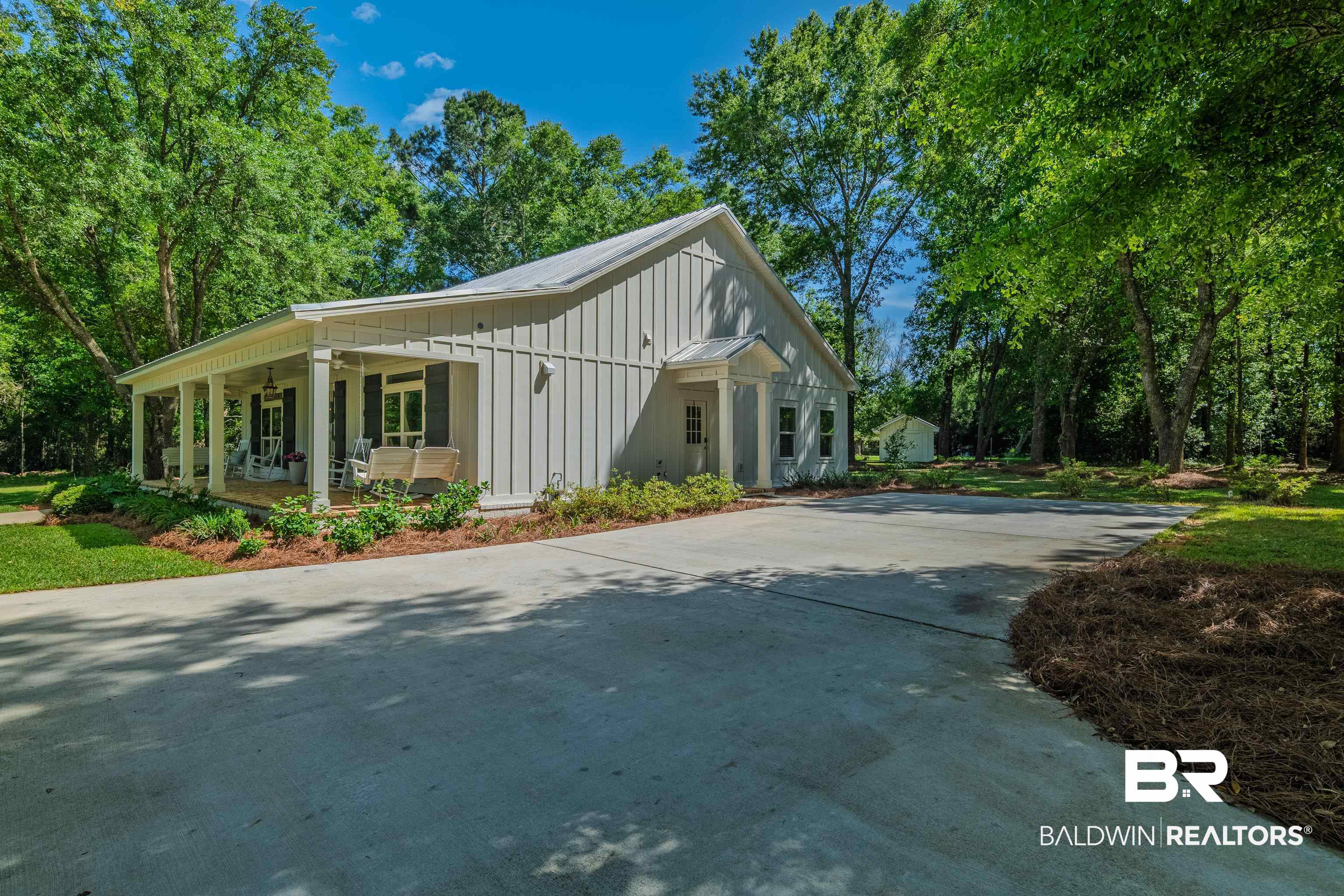 19121 Boothe Road Fairhope, AL 36532 - Photo 34 of 41 View of property exterior featuring a porch, concrete driveway, board and batten siding, a metal roof, and view of scattered trees