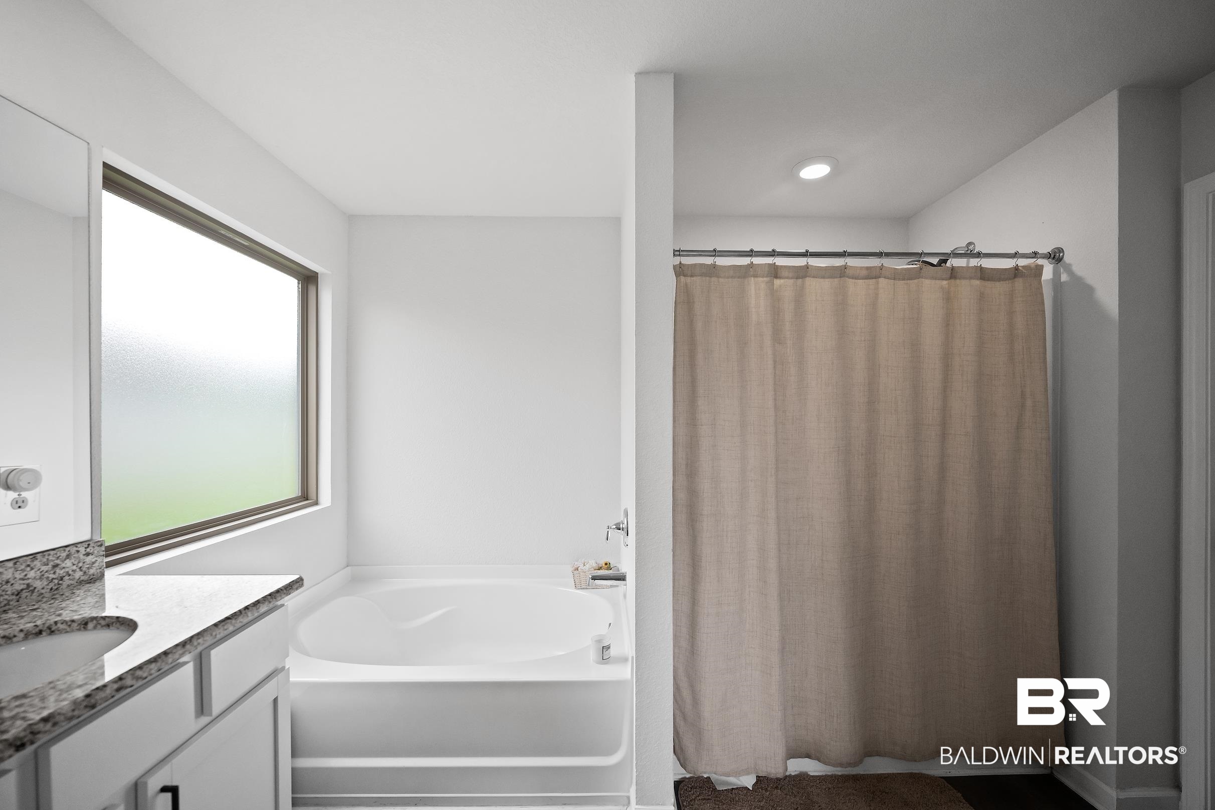 32030 Terranova Loop Lillian, AL 36549 - Photo 13 of 30 Bathroom featuring a large soaking tub with a privacy window, a built-in shower with a chrome rod, and a vanity with a stone-finish countertop