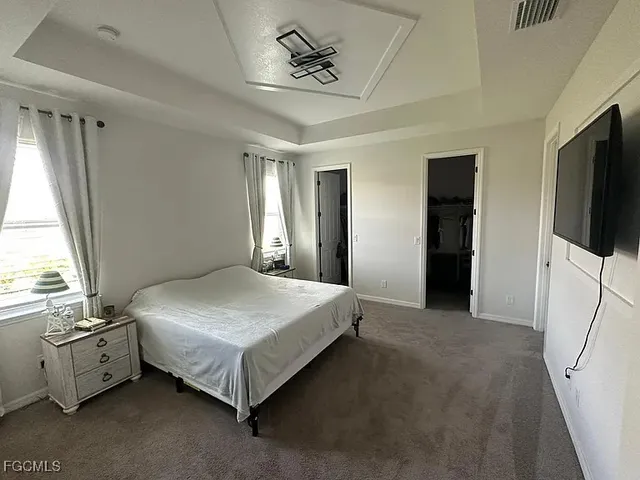 a spacious bedroom with a bed and a flat tv screen on dresser