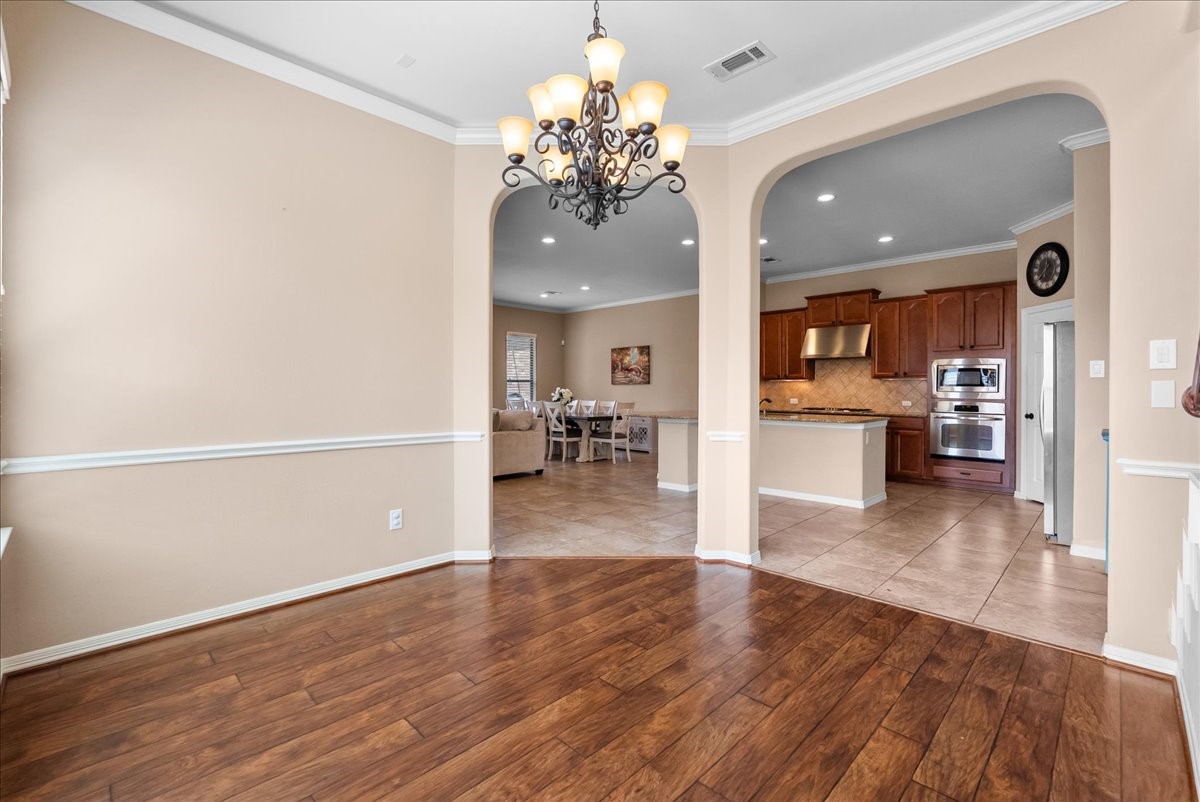 606 West Fork Webster, TX 77598 - Photo 8 of 46 Elegant formal dining room with rich hardwood floors and a classic chandelier, seamlessly flowing into the open kitchen and living area of this Edgewater, Webster home.