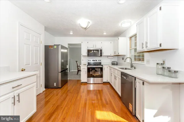 a kitchen with stainless steel appliances granite countertop a stove top oven a sink dishwasher and white cabinets with wooden floor