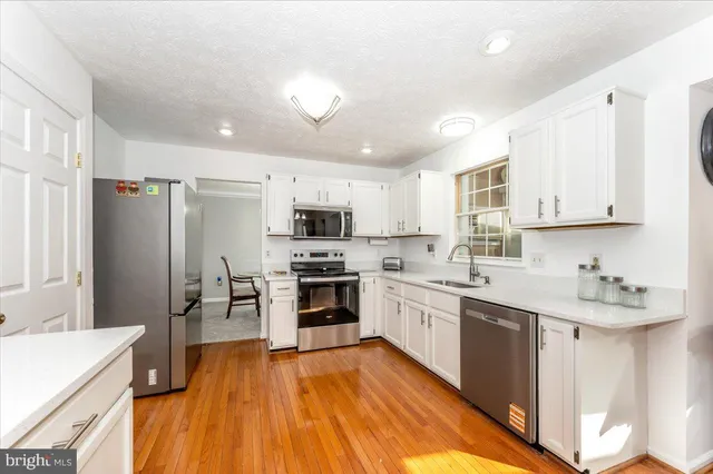 a large kitchen with stainless steel appliances granite countertop a refrigerator a sink dishwasher a stove and white countertops with wooden floor
