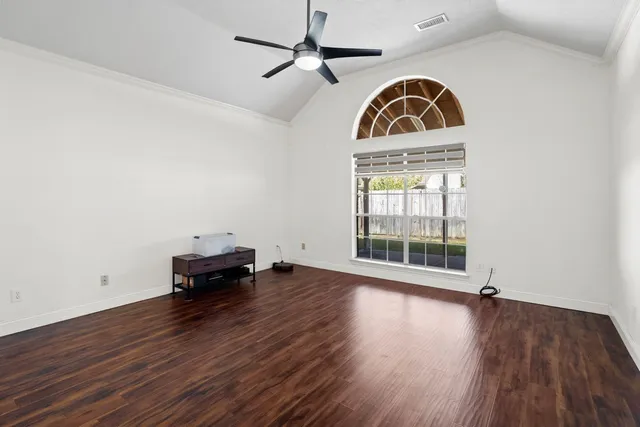 an empty room with wooden floor fan and windows