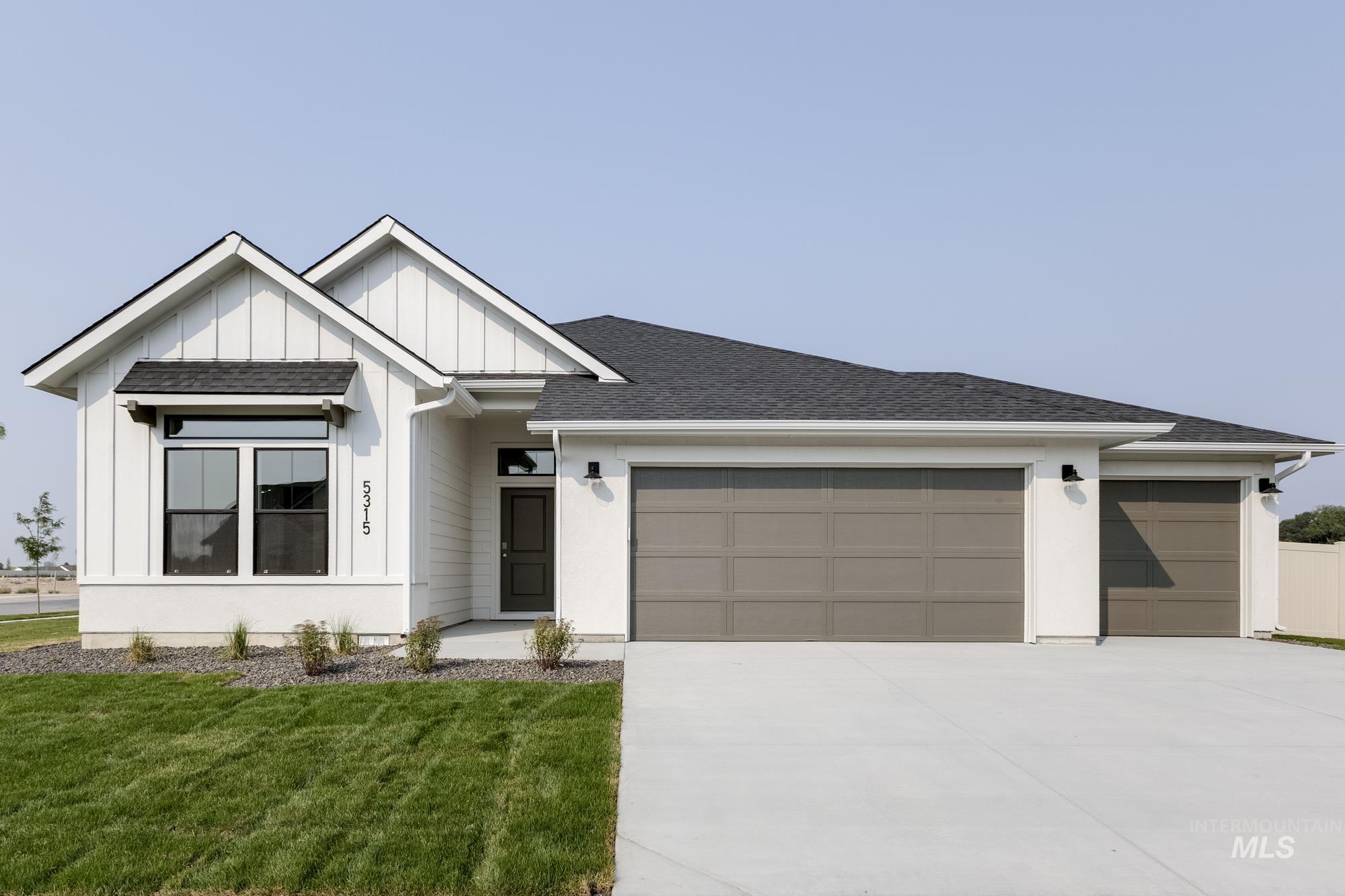 View of front of property with board and batten siding, an attached garage, driveway, a shingled roof, and a front lawn