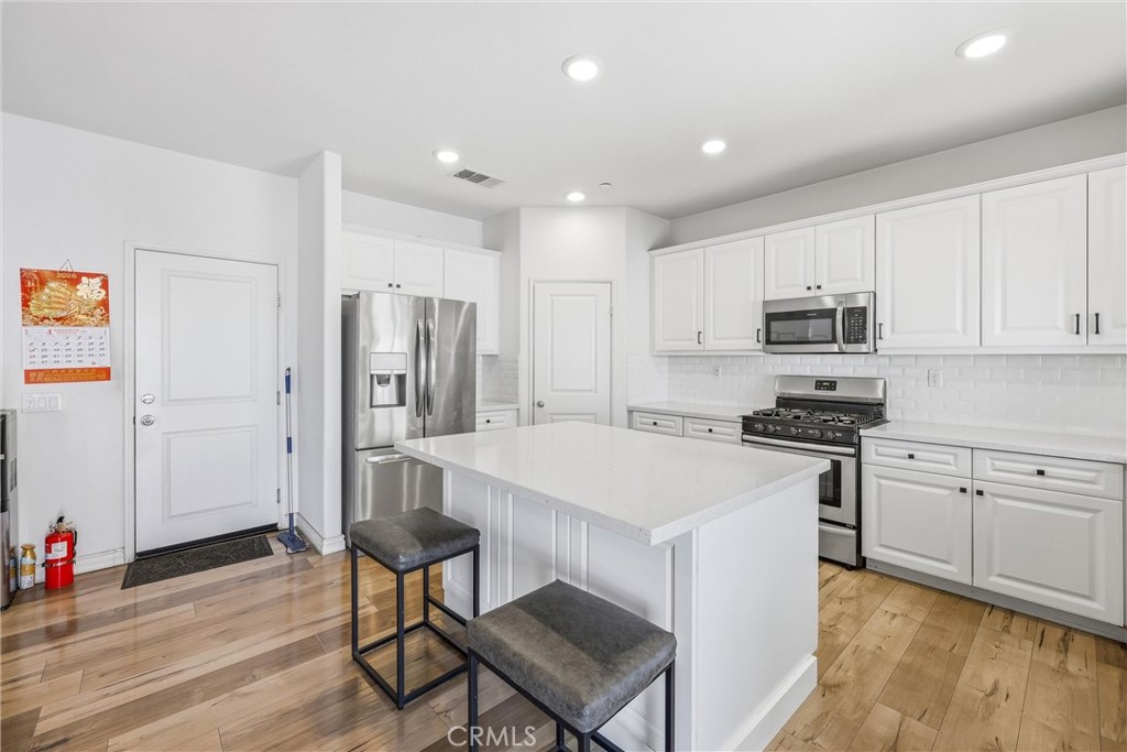 4783 Vanderham Way Eastvale, CA 91752 - Photo 12 of 29 a kitchen with stainless steel appliances a stove a sink a refrigerator white cabinets and wooden floor