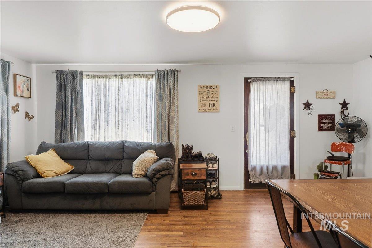 1958 East 1775 South Gooding, ID 83330 - Photo 9 of 49 Living area featuring wood-finish flooring, a large window with privacy sheers, a ceiling-mounted light fixture, white painted walls, and a wood-paneled door