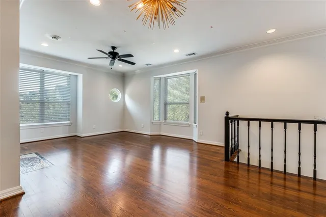an empty room with wooden floor chandelier fan and windows
