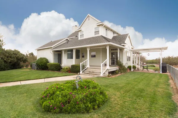 a white house with a large pool and lawn chairs next to a yard