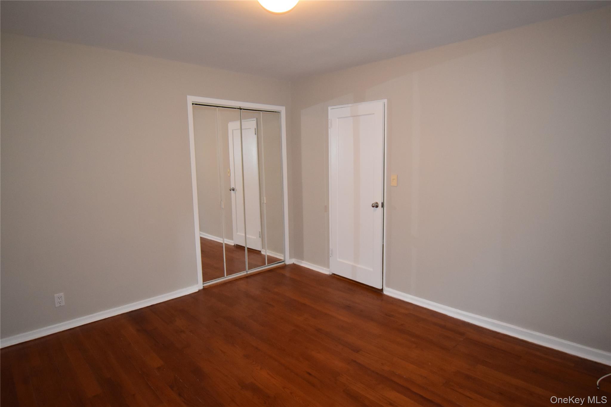 23 West Mill Drive, Unit 9A Great Neck, NY 11021 - Photo 11 of 12 Empty room featuring dark wood-style floors and baseboards
