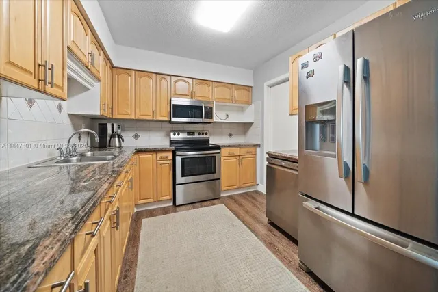 a kitchen with stainless steel appliances granite countertop a refrigerator a stove and a sink with wooden floor