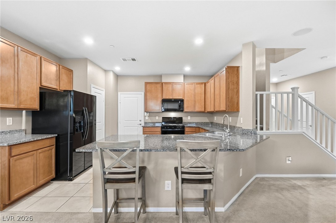 150 Fulgora Street Henderson, NV 89074 - Photo 26 of 92 Kitchen featuring breakfast bar, black appliances, dark stone counters and wood finish cabinetry.
