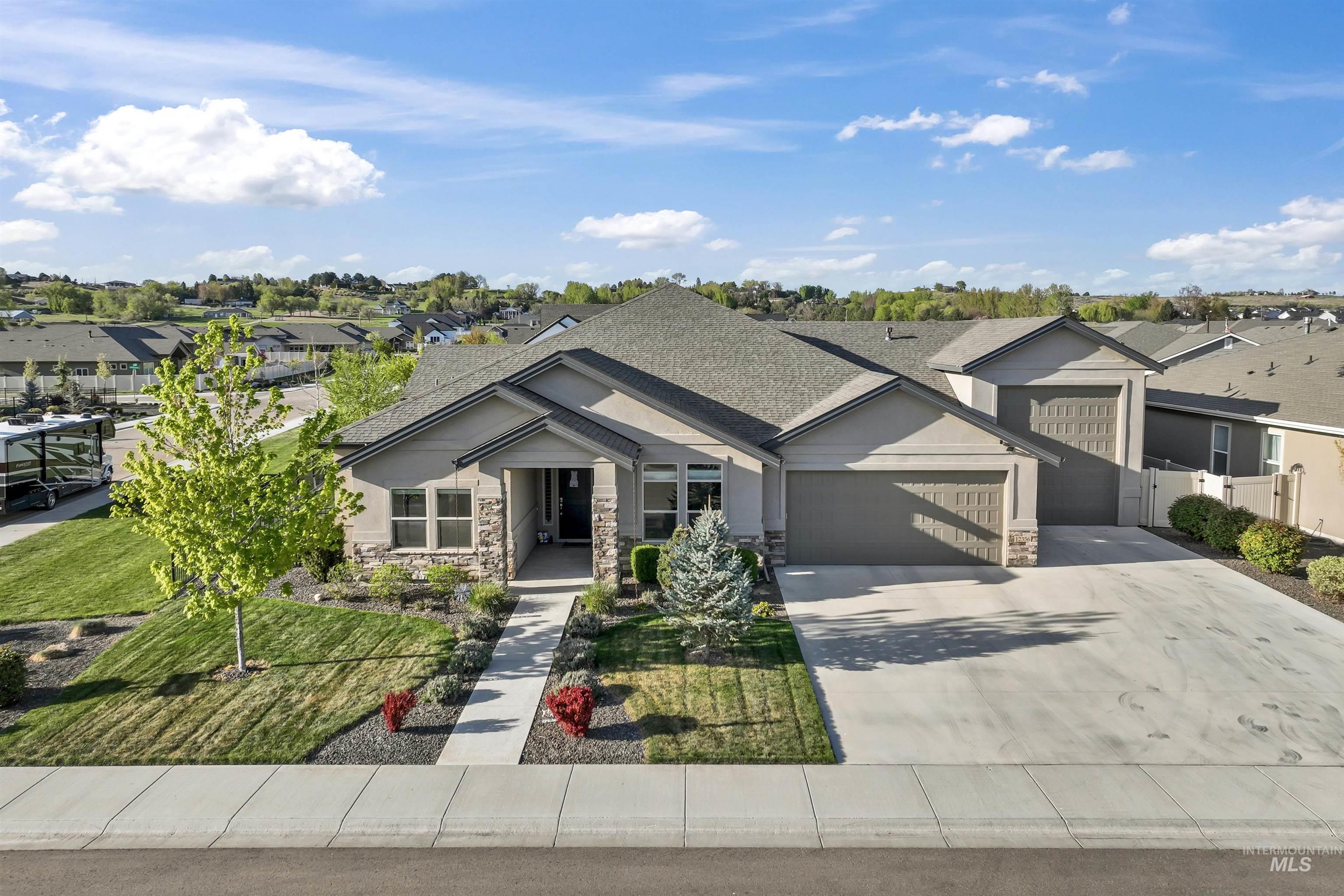 View of front of home featuring a garage, driveway, roof with shingles, stone siding, and a residential view