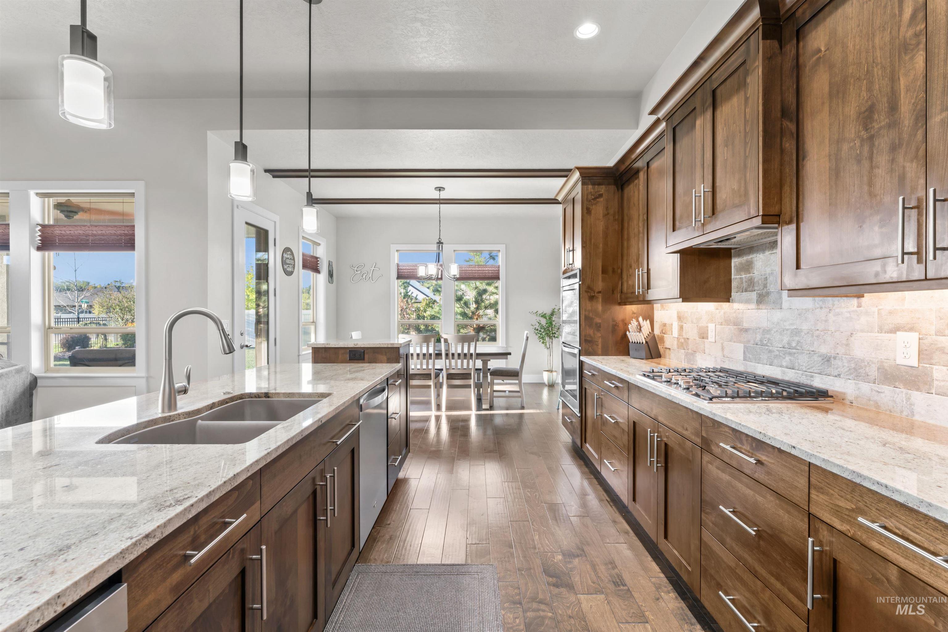 12356 West Rice Road Star, ID 83669 - Photo 11 of 49 Kitchen featuring hanging light fixtures, light stone counters, tasteful backsplash, dark wood-type flooring, and appliances with stainless steel finishes
