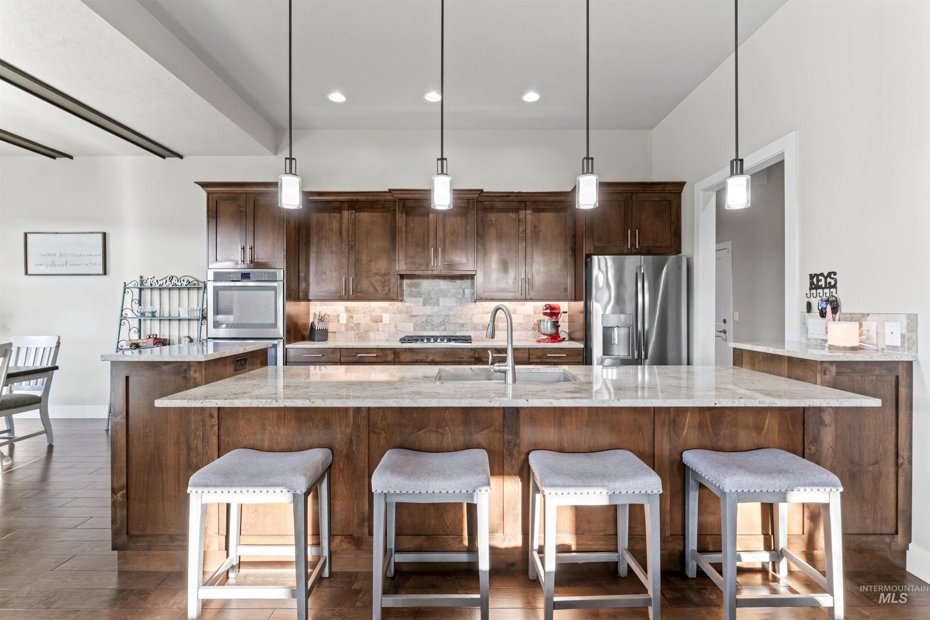 12356 West Rice Road Star, ID 83669 - Photo 8 of 49 Kitchen featuring backsplash, hanging light fixtures, light stone counters, a kitchen breakfast bar, and stainless steel appliances