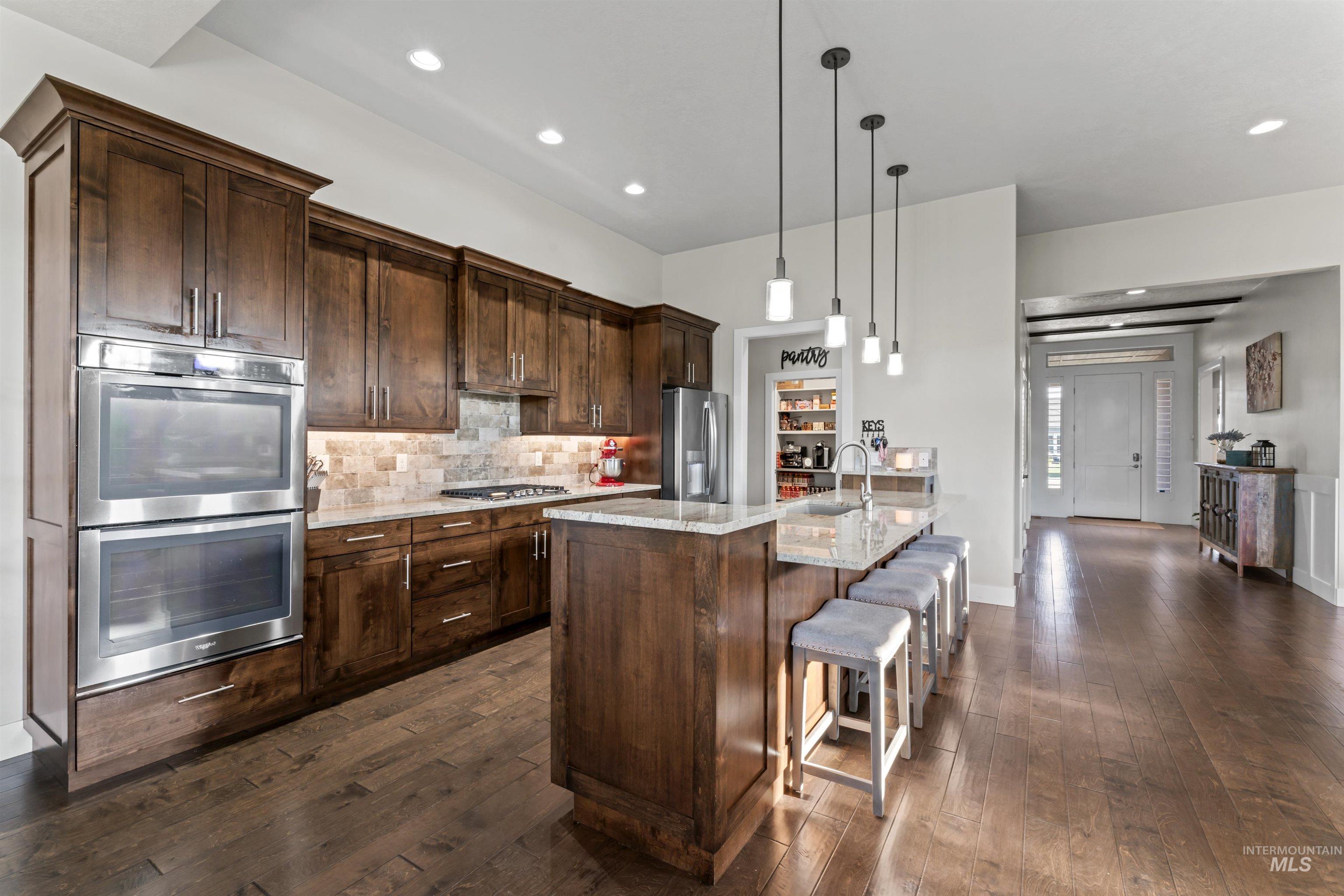 12356 West Rice Road Star, ID 83669 - Photo 9 of 49 Kitchen with light stone countertops, stainless steel appliances, hanging light fixtures, a breakfast bar, and tasteful backsplash