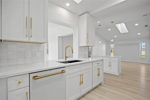 a kitchen with a sink dishwasher and white cabinets with wooden floor