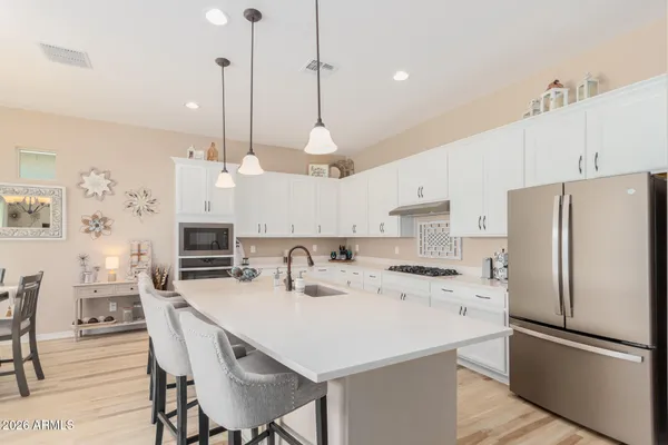 a kitchen with stainless steel appliances a stove a refrigerator a sink a dining table with chairs and white cabinets